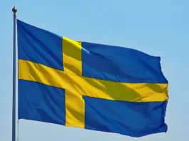 Sveriges flagga vajar i vinden mot klarblå himmel, med gult kors på blå botten.