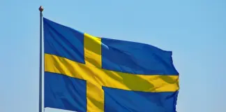 Sveriges flagga vajar i vinden mot klarblå himmel, med gult kors på blå botten.
