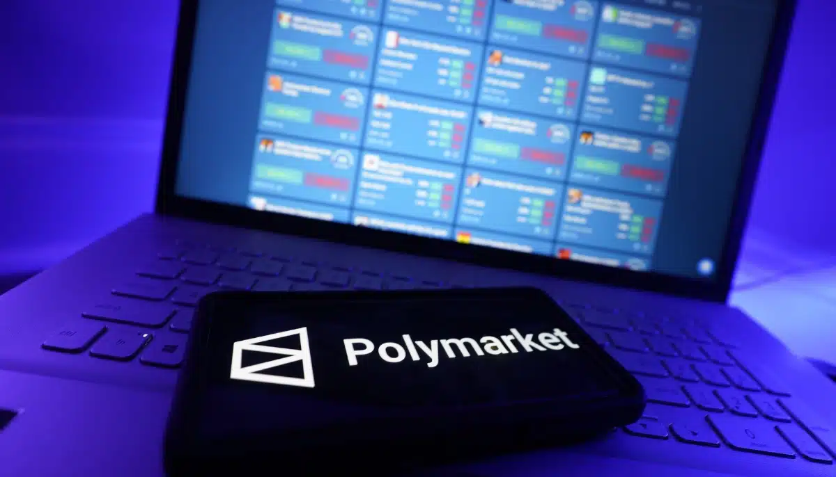 Polymarket-logotyp på mobil framför laptop med prediction market-översikt