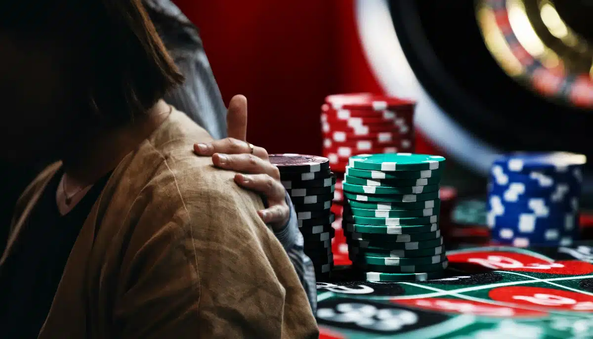 Person vid roulettebord med stödjande hand på axeln och spelmarker i bakgrunden