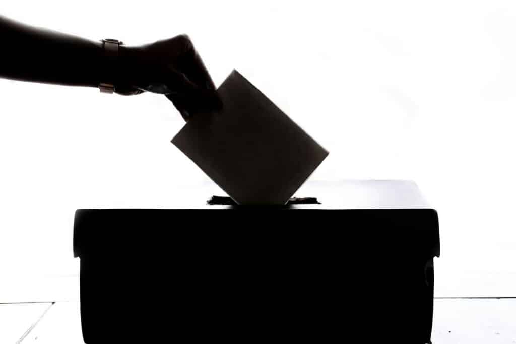 a shadowed hand placing a ballot in a voting box