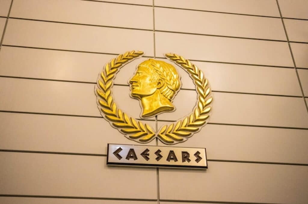 Caesars Entertainment logo featuring a gold laurel wreath and profile of Julius Caesar on a tiled wall.