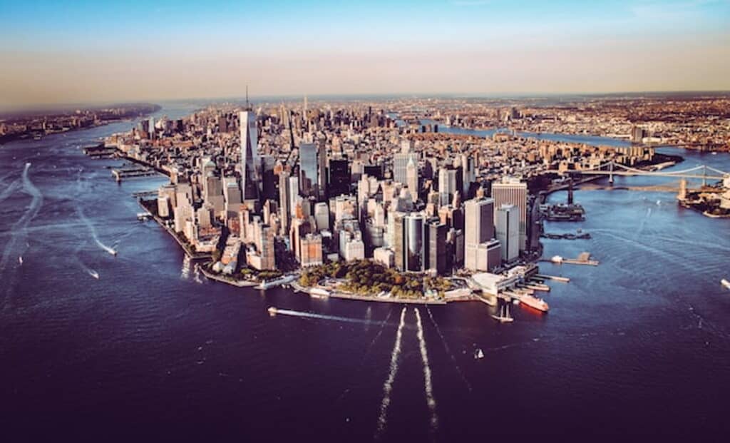Aerial view of Lower Manhattan skyline at sunset with surrounding rivers and bridges.
