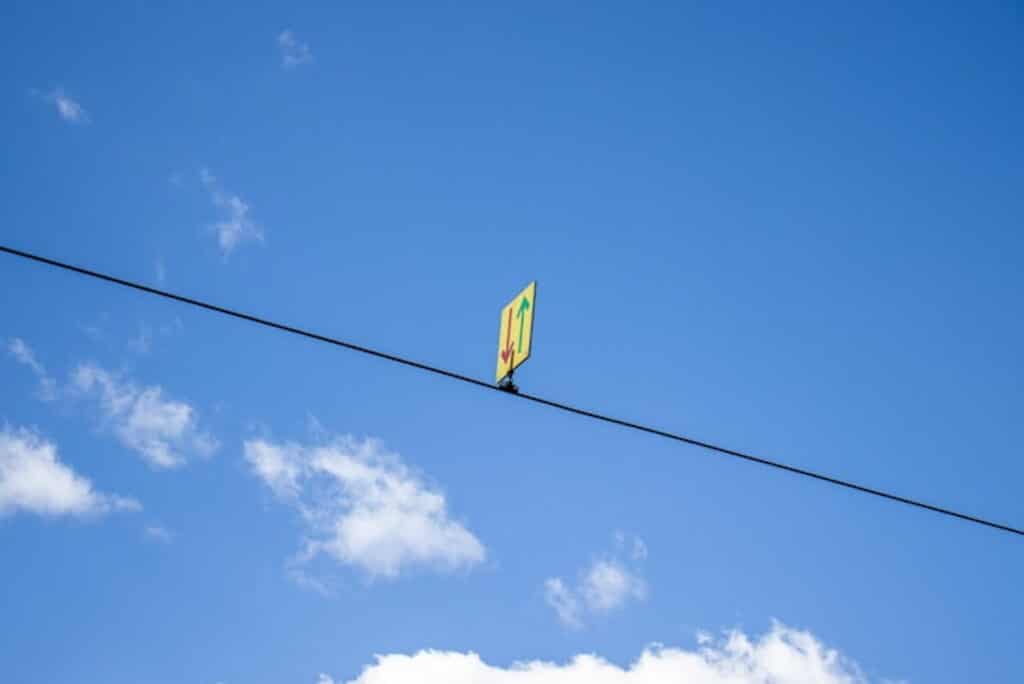 A two-way direction sign is attached to a wire against a blue sky with scattered clouds.