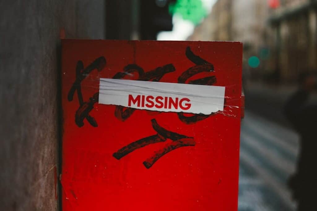 Red sign with the word “MISSING” taped on it in an urban street setting.