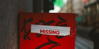 Red sign with the word “MISSING” taped on it in an urban street setting.