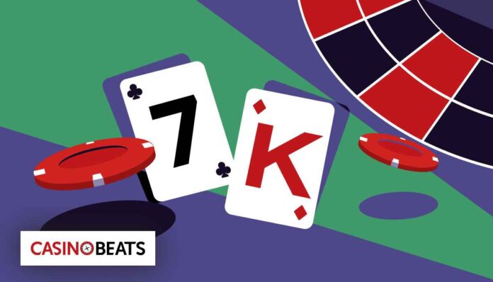 Two playing cards—7 of clubs and King of hearts—lie next to a red casino chip on a colorful gaming table.