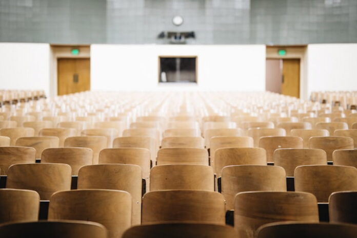 empty-college-lecture-hall.jpg Empty college lecture hall with rows of wooden chairs facing a podium