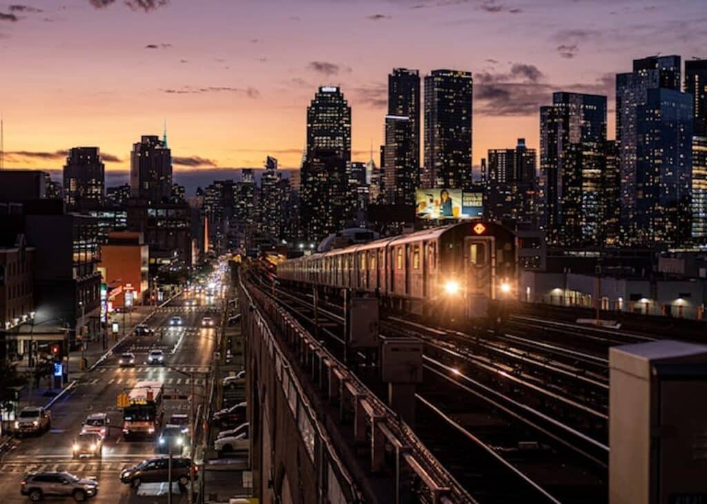 NYC 7 train approaching at sunset with the Long Island City skyline in the background.