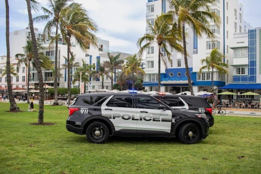 Police SUVs parked on grass in front of palm trees and art deco buildings