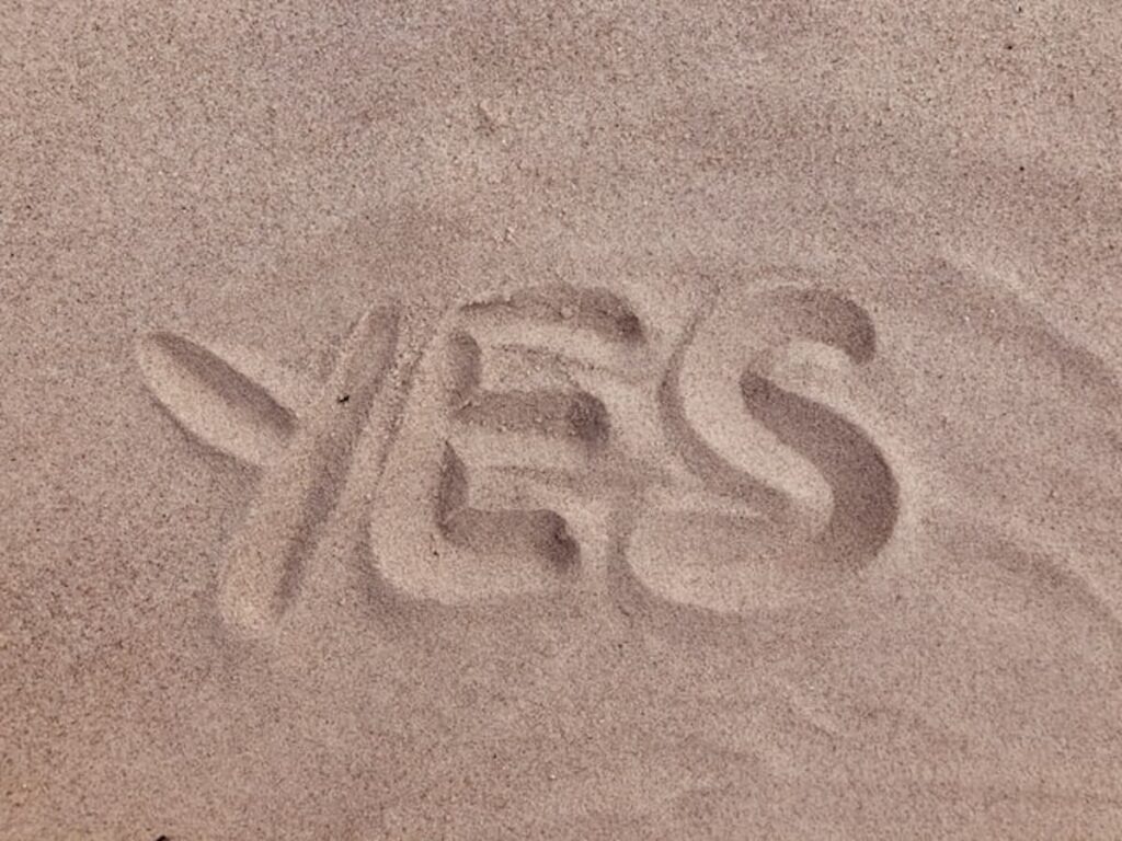 The word "YES" written in smooth, light brown beach sand.
