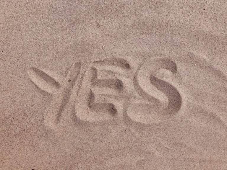 The word "YES" written in smooth, light brown beach sand.