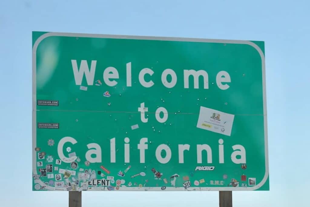 Green roadside "Welcome to California" sign with stickers.