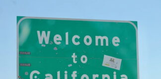 Green roadside "Welcome to California" sign with stickers.