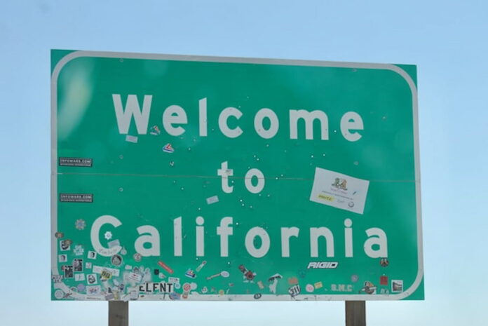 Green roadside "Welcome to California" sign with stickers.