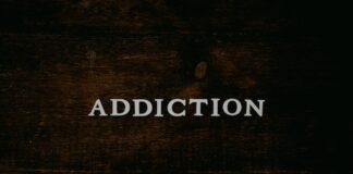 Word “Addiction” displayed on a dark wooden surface