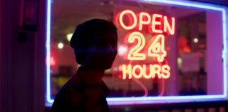 Neon sign reading “Open 24 Hours” outside a storefront at night.