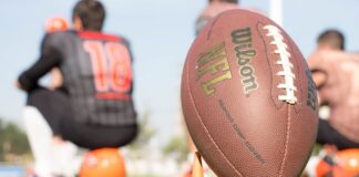 Close-up of a football on a tee with blurred players in the background
