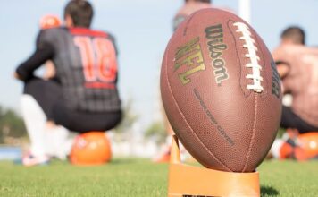 Super Bowl 60 Odds: Bettor Makes $1K MVP Wagers on Seattle & New England Kickers Close-up of an NFL football on a tee with blurred players in the background