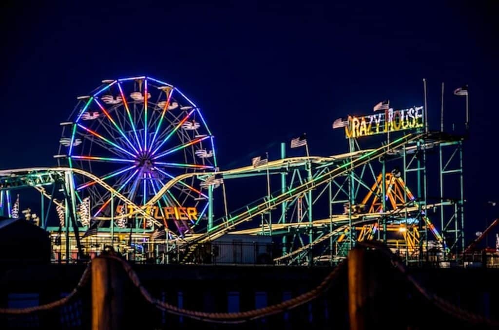 Colorful Ferris wheel and roller coaster lights glowing at night on the Atlantic City Steel Pier boardwalk.