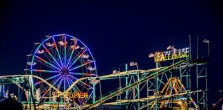 Colorful Ferris wheel and roller coaster lights glowing at night on the Atlantic City Steel Pier boardwalk.