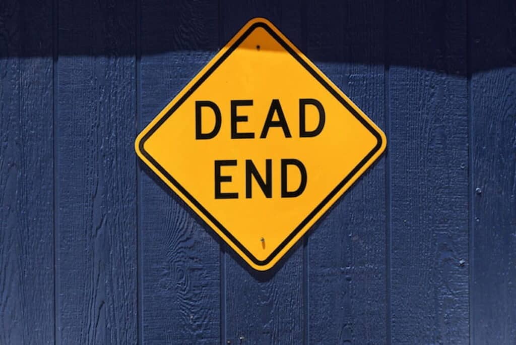 Yellow diamond-shaped “Dead End” road sign mounted on a dark blue wooden wall.