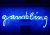 Bettors Favor DraftKings Over Kalshi, Truist Survey Says Blue neon sign spelling the word gambling on a wall with domino patterns.
