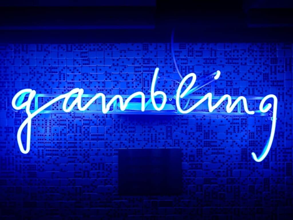 Blue neon sign spelling the word gambling on a wall with domino patterns.