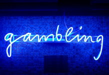 Blue neon sign spelling the word gambling on a wall with domino patterns.