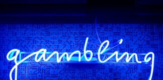 Blue neon sign spelling the word gambling on a wall with domino patterns.