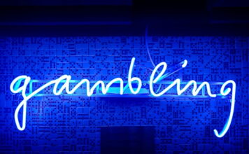 Blue neon sign spelling the word gambling on a wall with domino patterns.