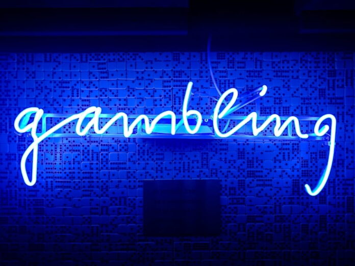 AGA Survey Finds 85% of Americans View Prediction Markets as Gambling Blue neon sign spelling the word gambling on a wall with domino patterns.