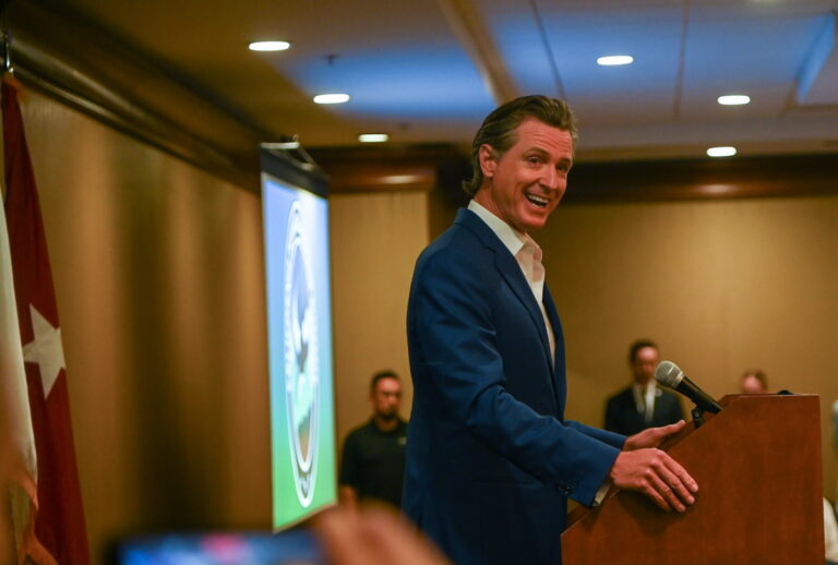Gavin Newsom speaking at a podium during the California Defense Leadership Summit in Sacramento