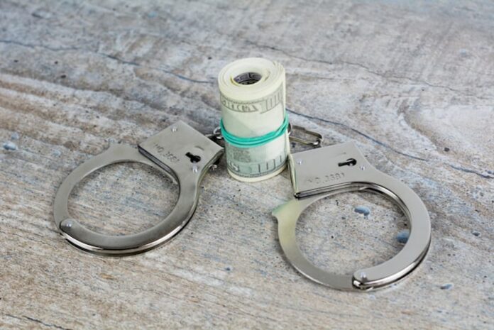 Handcuffs next to a rolled stack of cash on a wooden surface