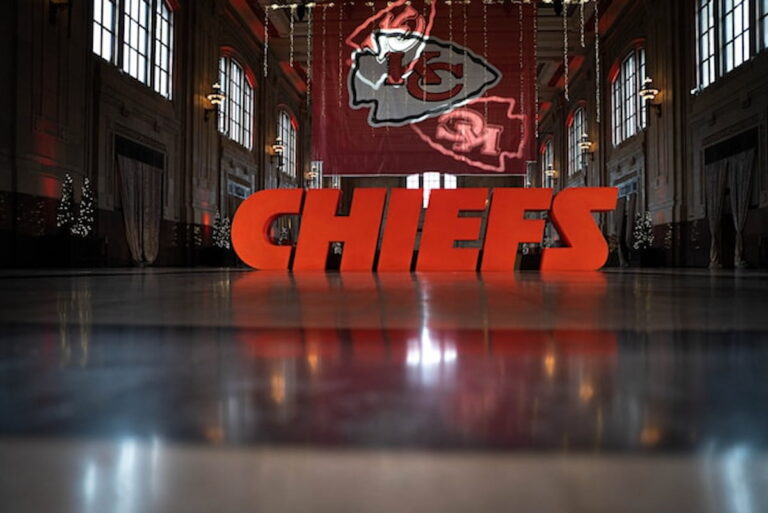 Large CHIEFS sign displayed inside a historic hall with Kansas City Chiefs logo in the background