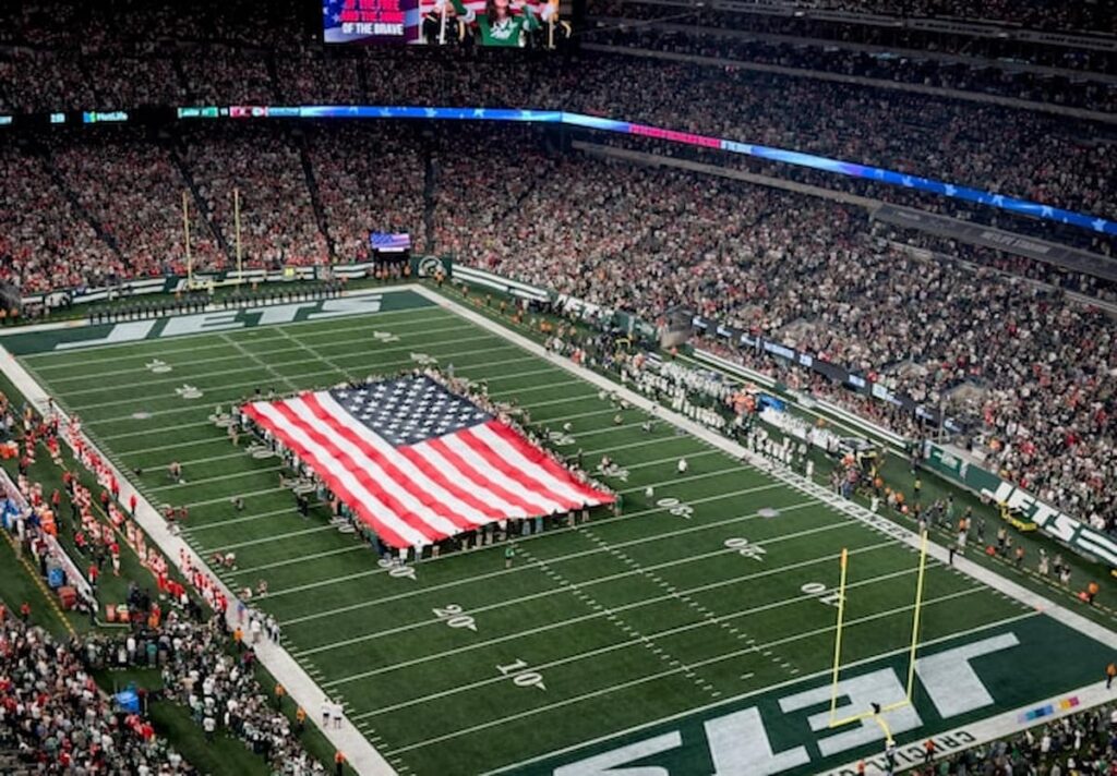 A large American flag displayed on the field during a packed NFL game.