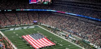 A large American flag displayed on the field during a packed NFL game.