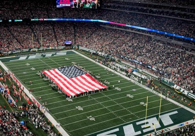 A large American flag displayed on the field during a packed NFL game.