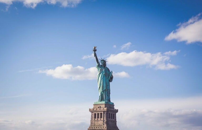 The Statue of Liberty against a bright blue sky with scattered clouds