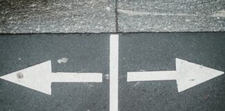 White arrows painted on asphalt pointing in opposite directions, symbolizing choice and decision.