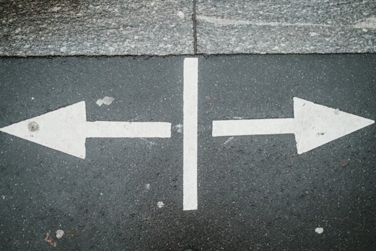White arrows painted on asphalt pointing in opposite directions, symbolizing choice and decision.