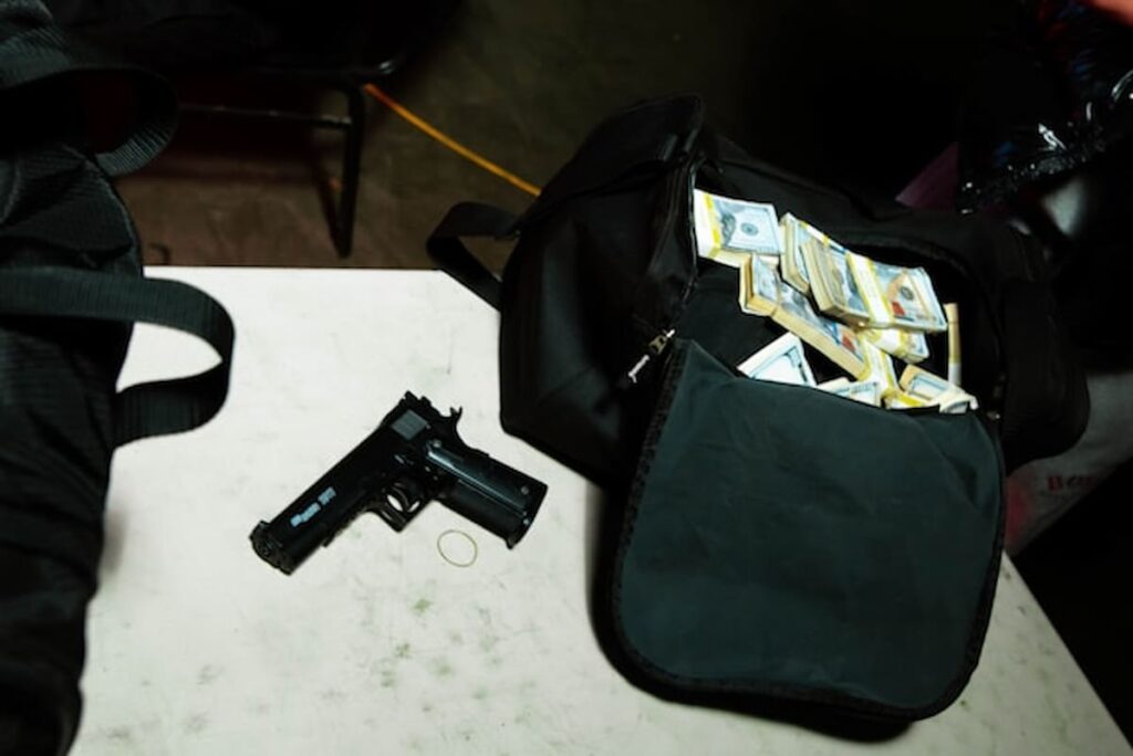Handgun and duffel bag filled with stacks of cash on a table