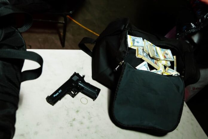 Handgun and duffel bag filled with stacks of cash on a table