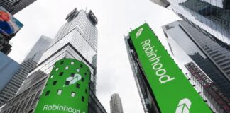 Robinhood Looking to Make Prediction Market Acquisition Tall glass buildings with large digital billboards in a city center.