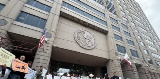 People gathered outside a large government building holding signs during a public demonstration.