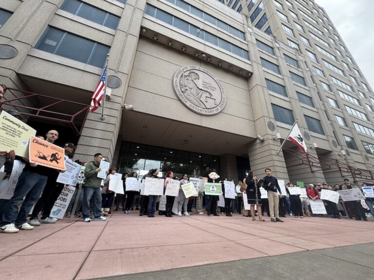 People gathered outside a large government building holding signs during a public demonstration.