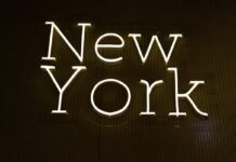 New York Bill Proposes Ban on Sports Prediction Markets Bright neon-style sign spelling out “New York” on a dark wall background.