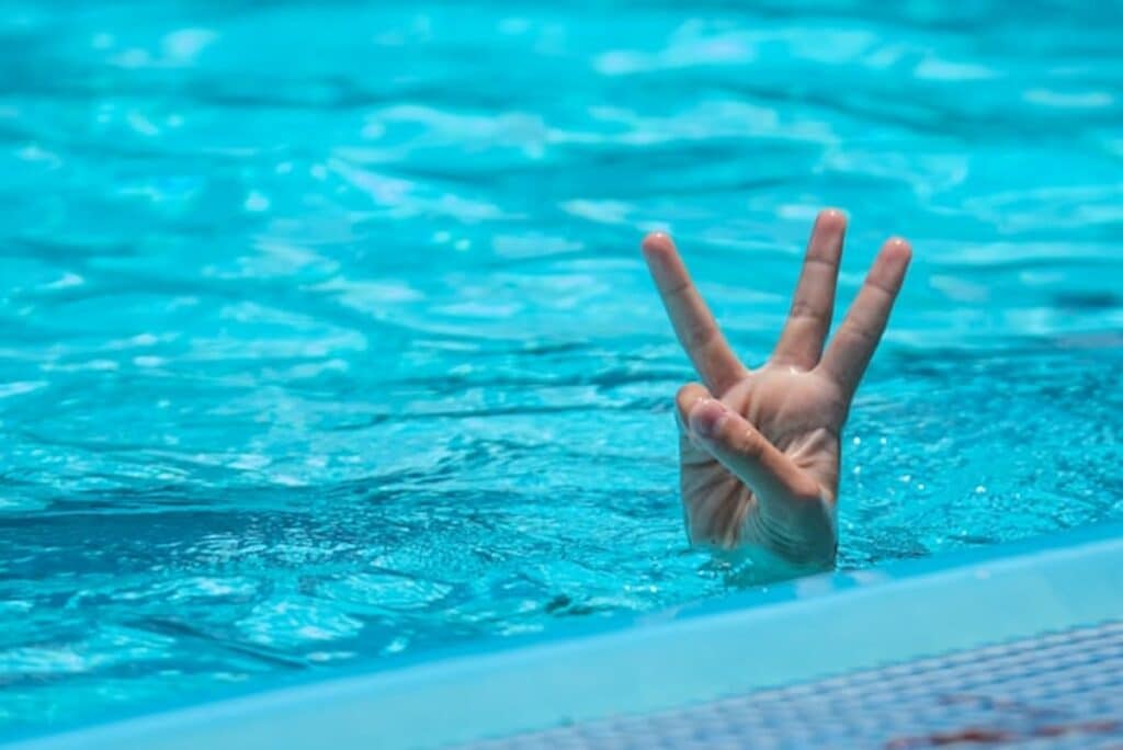 Hand showing three fingers above a swimming pool surface