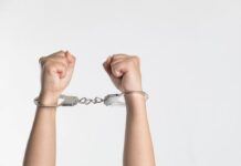 Close-up of hands in handcuffs raised upward.