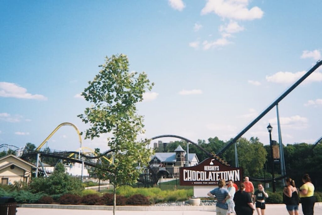Visitors walk near the Hershey’s Chocolatetown entrance and roller coasters on a sunny day in Hershey, Pennsylvania.